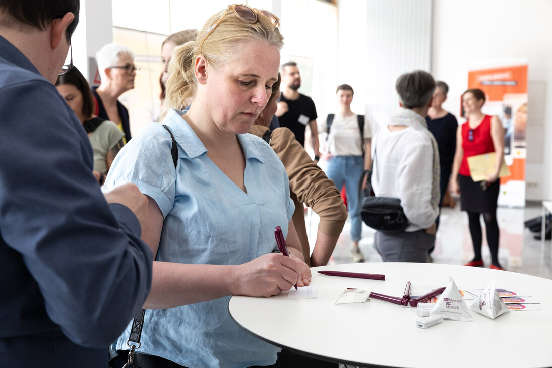 Frau steht am Stehtisch während der Veranstaltung und schreibt etwas auf einen Zettel